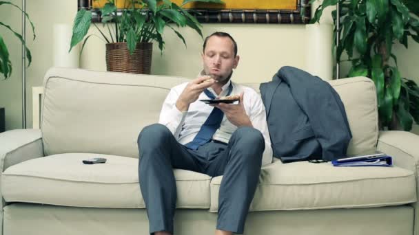 Zakenman eten boterham op sofa thuis — Stockvideo