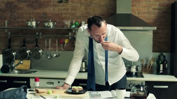 Empresário comendo sanduíche e lendo jornal na cozinha — Vídeo de Stock