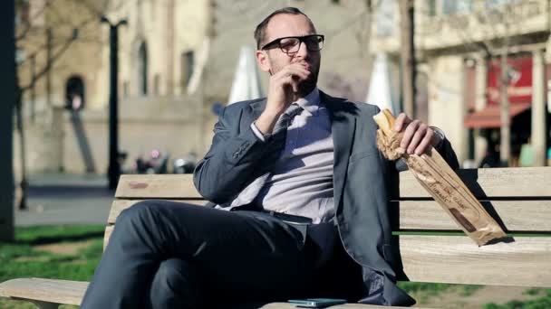 Joven hombre de negocios guapo comiendo baguette en la ciudad — Vídeo de stock