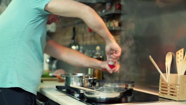 Kızartma tavası mutfakta yemek için baharat ekleyerek adam — Stok video