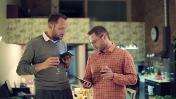 Zwei Freunde mit Smartphones reden und trinken auf Party Wein — Stockvideo