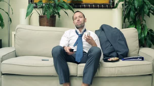 Empresario viendo la televisión y tomando café en el sofá en casa — Vídeos de Stock