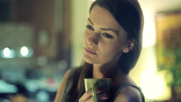 Ledsen, vacker kvinna dricker kaffe vid fönstret på natten — Stockvideo