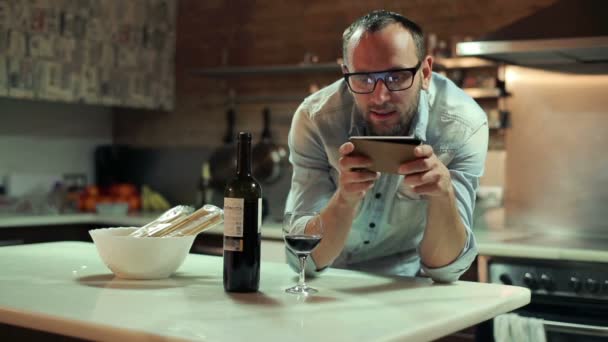 Junger glücklicher Mann mit Smartphone trinkt Wein in der heimischen Küche — Stockvideo