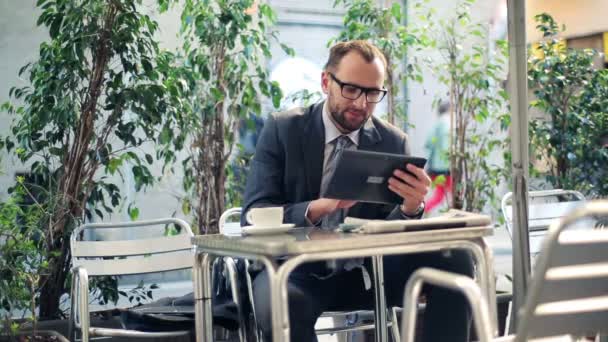 Молодой бизнесмен с планшетным компьютером в открытом кафе — стоковое видео