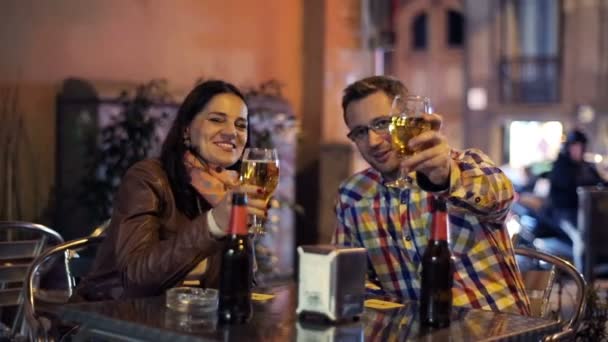 Pareja joven brindando por la cámara en el bar al aire libre por la noche — Vídeos de Stock