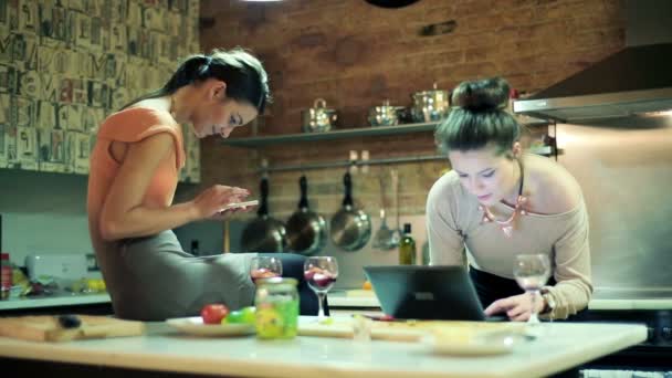 Two girlfriends with smartphone and laptop in the kitchen — Stock Video