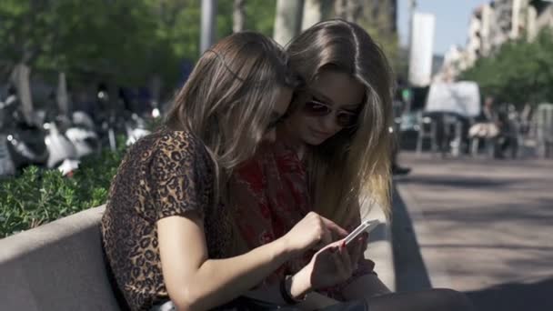 Girlfriends with smartphone sitting on bench in the city — Stock Video