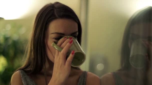 Грустная, красивая женщина пьет кофе у окна ночью — стоковое видео