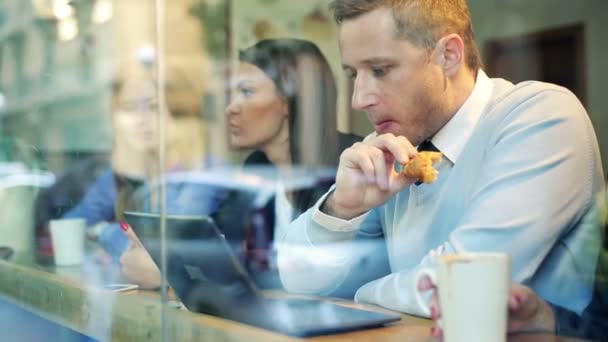 Hombre de negocios con portátil, mujer de negocios con teléfono inteligente sentarse en la cafetería — Vídeos de Stock