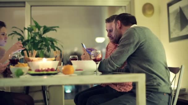 Amigos con smartphone sentados junto a la mesa por la noche — Vídeos de Stock