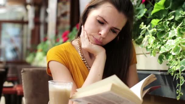 Joven leyendo libro, bebiendo jugo en la cafetería — Vídeos de Stock