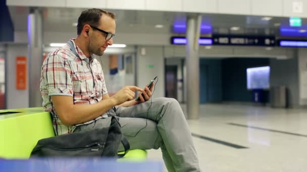 Mladý muž poslouchat hudbu na smartphone na železniční terminál — Stock video