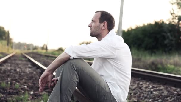 Грустный, сердитый человек, сидящий на железной дороге — стоковое видео