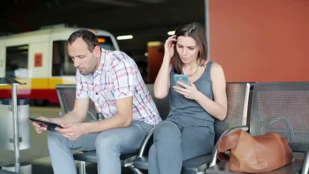 Passengers with smartphone and tablet waiting at train station — Stock Video