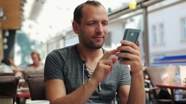 Retrato de joven feliz hombre con teléfono inteligente sentado en el restaurante — Vídeo de stock