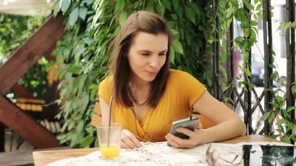Mujer escuchar música en el teléfono inteligente, beber jugo en la cafetería — Vídeo de stock