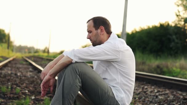 Сумний, злий чоловік сидить на залізничній колії — стокове відео