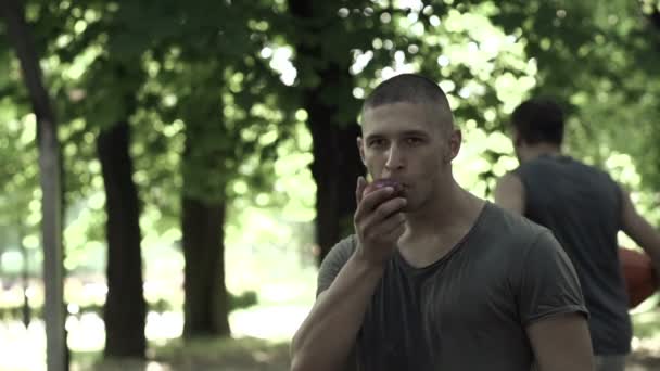 Hombre comiendo manzana en cancha de baloncesto — Vídeo de stock