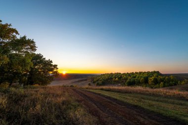Şafakta sabah güneşi. Sonbahar ormanını ve yolu aydınlattı.