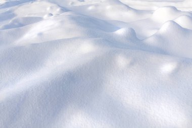 Kış sezonu sahnesi. Parlak güneş ışığında kar dalgalarının dokusu. Doğal bir yüzeyi var. Telif uzayı, kum tepelerinin ve kar tanelerinin arka plan şablonu