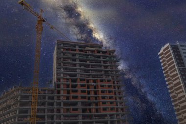 Uzun vinç, binalar ve geceleri Samanyolu. İnşaat vinci, bitmemiş ev için çimentoyla beton konteynırı kaldırır..