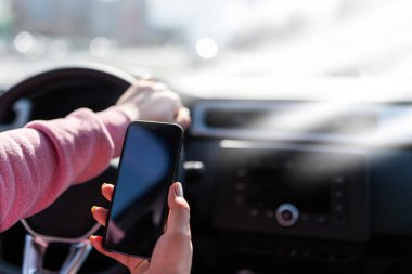 El telefonu arabanın direksiyonunun arka planına doğru tutar. Cep telefonuyla dikkati dağılmış sürücü. Yazı ya da resim için boş siyah ekranlı bir telefon. Kaza tehlikesi. 