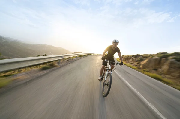 Велогонщик катается на горном велосипеде в солнечный день по горной дороге — стоковое фото
