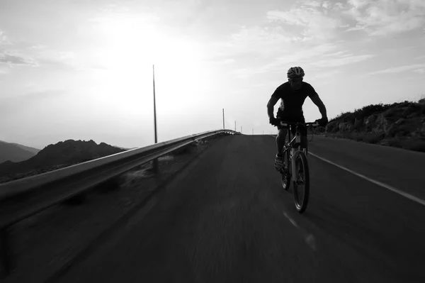 Ciclista homem montando montanha em uma estrada de montanha, silhueta sunri — Fotografia de Stock