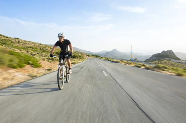 Cyclist man riding mountain bike in sunny day on a mountain road — Stock Photo, Image