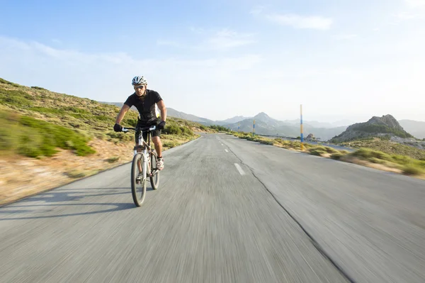 Ciclista homem montando bicicleta de montanha em dia ensolarado em uma estrada de montanha — Fotografia de Stock