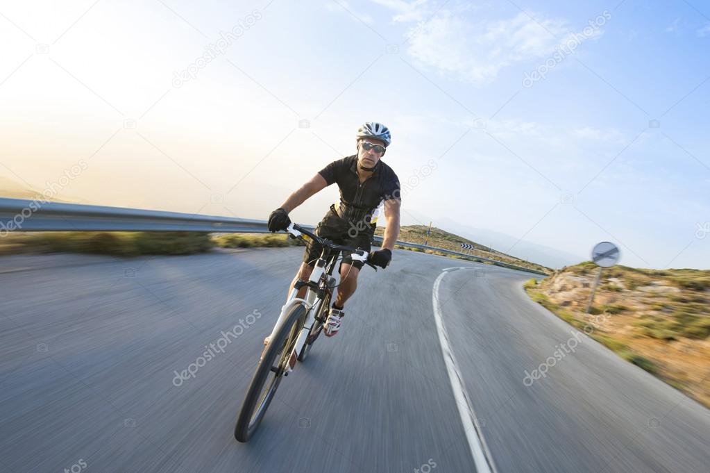 Cyclist man riding mountain bike in sunny day on a mountain road