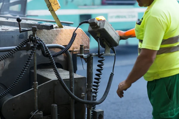 Werknemer die asfalt bestratingsafwerkmachines machine tijdens de aanleg van wegen en herstellen werkt — Stockfoto