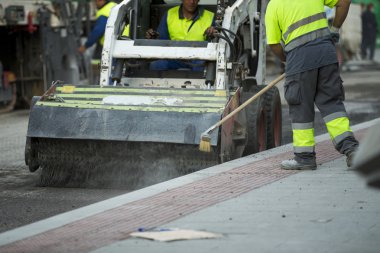 Worker operating asphalt paver machine during road construction and repairing works clipart