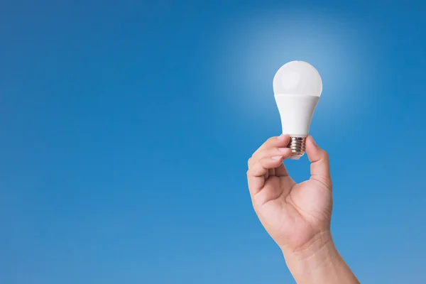 Ampul LED aydınlatma ile mavi gökyüzü arka plan üzerinde tutan el.