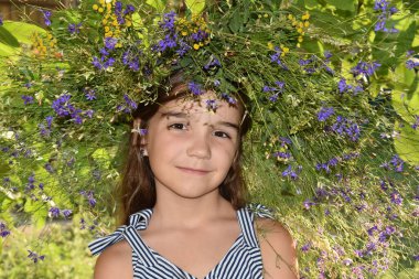 Çizgili elbiseli bir kız ve başında bir çelenk, gülümsüyor.