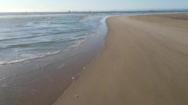 Yüksek açılı deniz manzarası arka planda teknelerle sahile doğru akıyor.