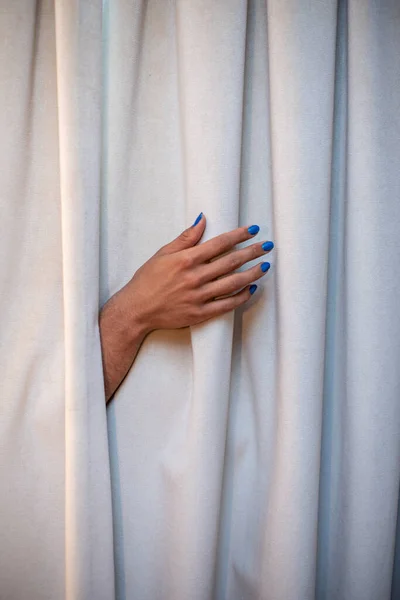 Рука торчит из занавески с синим лаком для ногтей — стоковое фото