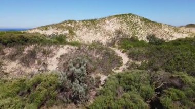 Ufukta okyanus olan kum tepeciklerine doğru uçan dronun sinematik yaklaşımı