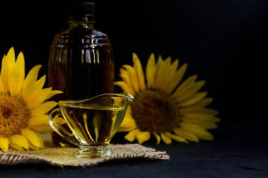 Ayçiçeği yağı cam tencereye döküldü. Branda peçetenin üzerinde duruyordu. Siyah arka planda çiçekler ve şişenin yanında.