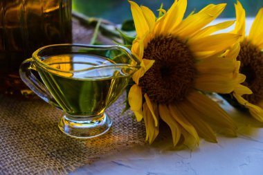 Cam tencereye dökülen ayçiçeği yağı bir peçetenin üzerindedir. Bir şişe yağ ve çiçeğin yanında. beyaz arkaplan