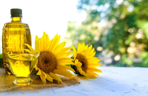 Aceite de girasol vertido en una cacerola de vidrio está en una servilleta de lona. cerca de una botella de aceite y flores. sobre fondo blanco Imagen De Stock