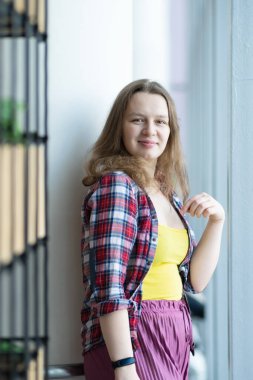 Ekose gömlekli kız alışveriş merkezinin penceresinin yanında duruyor. Düşünceli bakış. Yeşil bir çiçek tarhında.