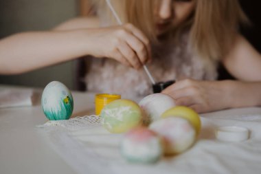 Paskalya çocukları yaratıcılığı arttırır. Küçük kız beyaz bir yumurta boyuyor. Diğer yumurta ve tavşanların yanında.