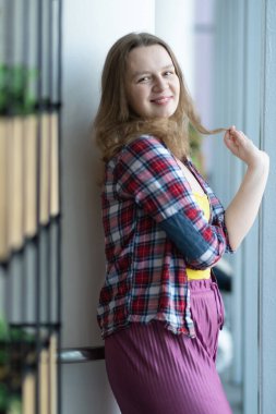 Ekose gömlekli kız alışveriş merkezinin penceresinin yanında duruyor. Düşünceli bakış. Yeşil bir çiçek tarhında.