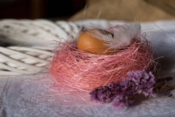 Červené vejce v slámovém hnízdě na lehkém, jemném pozadí. jasná velikonoční dovolená v rustikálním stylu. — Stock fotografie