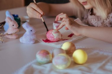 Paskalya çocuklarının yaratıcılığı. Küçük bir kız beyaz yumurta boyuyor. Diğer yumurta ve tavşanların yanında.