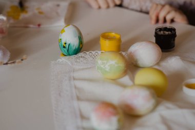 Paskalya çocuklarının yaratıcılığı. Küçük bir kız beyaz yumurta boyuyor. Diğer yumurta ve tavşanların yanında.