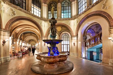 Viyana 'nın Palais Ferstel kentinde, ziyaretçiler süslü Tuna Çeşmesi' nin yanından geçerek tarihi atari salonunun tadını çıkararak bir kafede yemek yiyorlar..