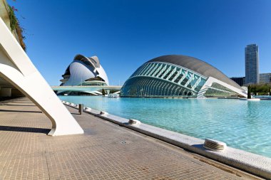 İspanya 'nın Valencia kentindeki Hemisferic nehrinin yanından geçen insanlar, açık mavi gökyüzü ve sakin su yansımaları ile öğleden sonra boyunca yürür..